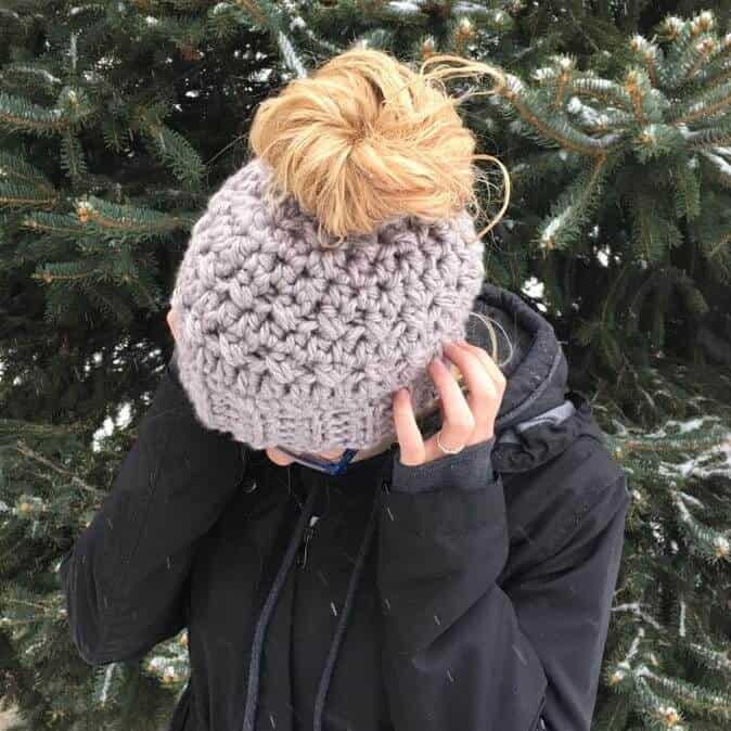 Photo showing the top view of the crocheted messy bun hat worn by a woman wearing a black jacket