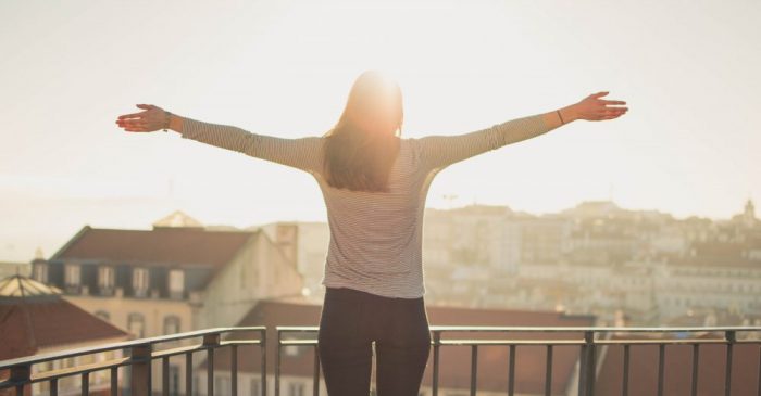 Photo of the back of a woman with her arms spread enjoying the sun