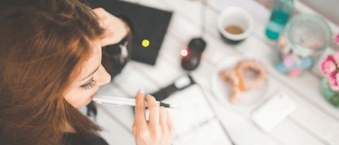 Top view photo of a woman holding a pen on her lips with a table full of stuff 