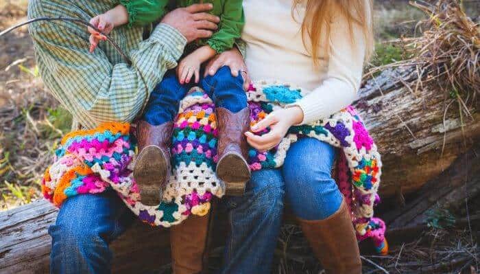 Photo of a family, their laps covered in a colorful crocheted blanket