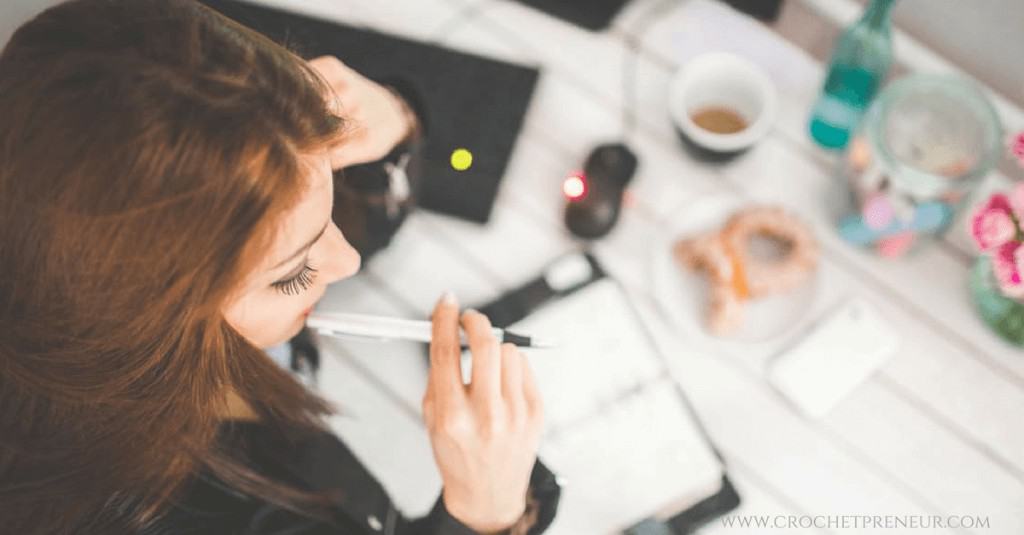 A top view photo of a woman holding a pen on her lips with a planner on her desk