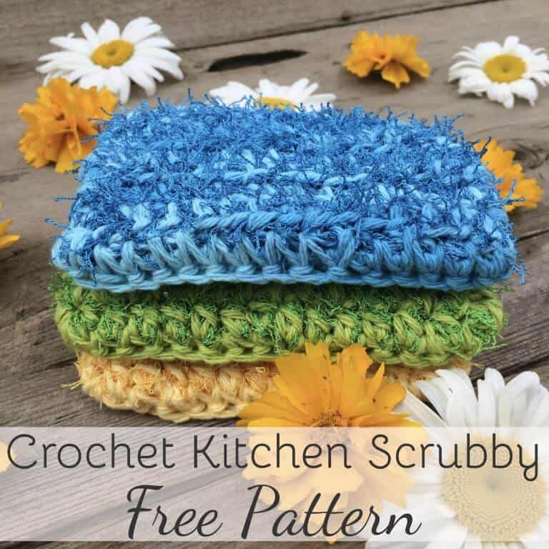 3 Kitchen Scrubbies in blue, green, and cream color on top of a wooden table surrounded with flowers