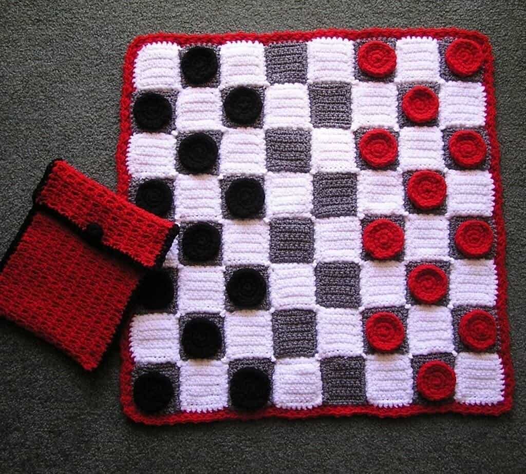 Photo of a crocheted checker board with black and red pieces with a red and black pouch