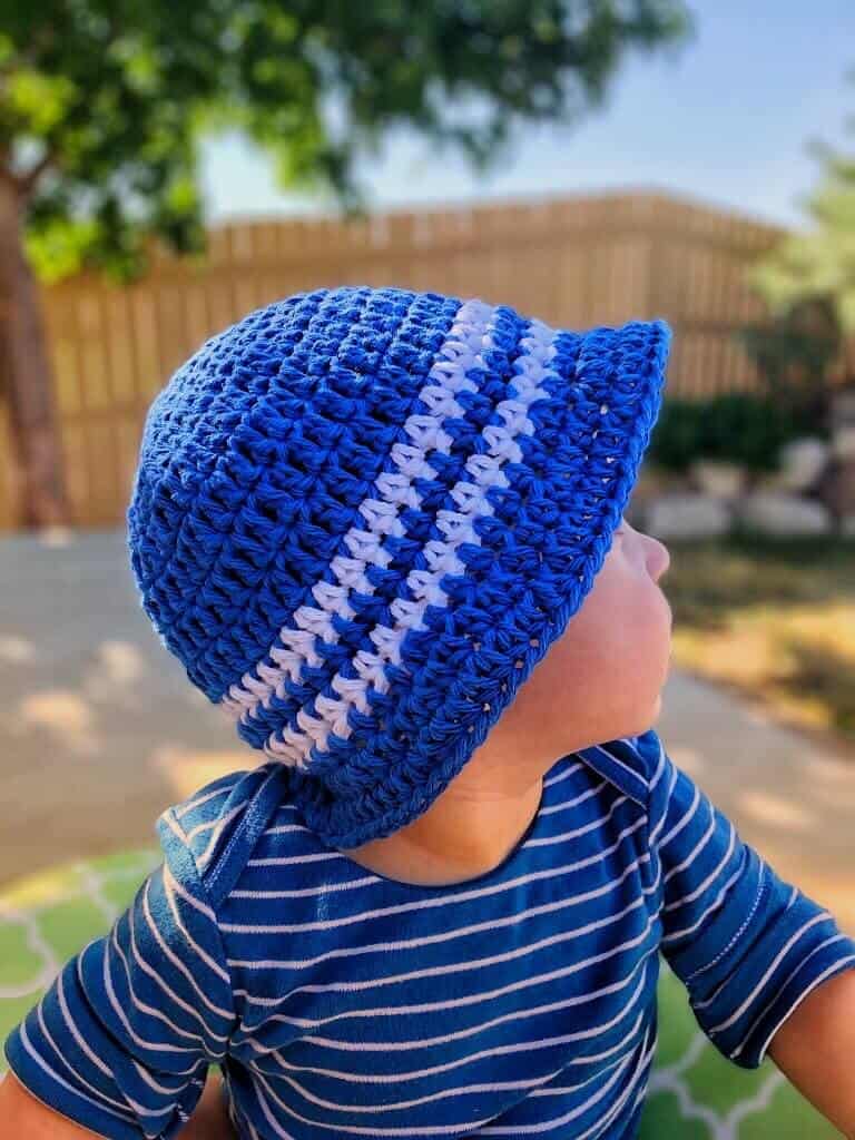 Blue with white stripes Sun and Sand Little Boys Bucket Hat worn by a kid with blue and white shirt looking away from the camera