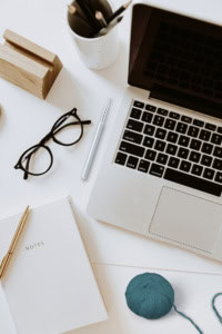 Share your crochet designs - image of a workspace with a laptop, notebook, glasses, crochet hook, and yarn