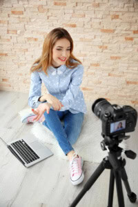 How to Start a Blog for Your Etsy Shop - image of a woman using a laptop, sitting in front of a camera on a tripod