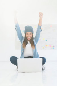 tips for online business success - image of a woman using a laptop, smiling, and raising her arms in celebration