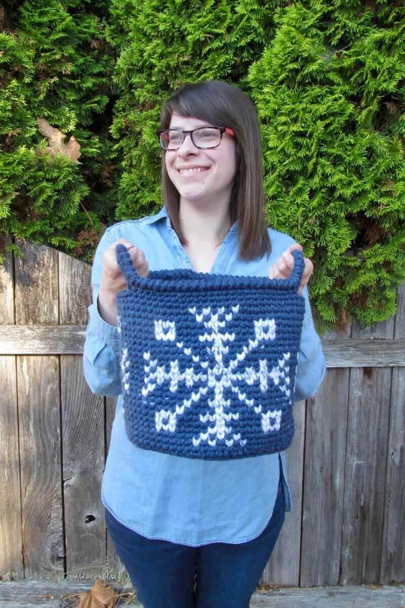 A photo of Sarah LarRieu holding the blue crocheted Let it Snow Tapestry Basket