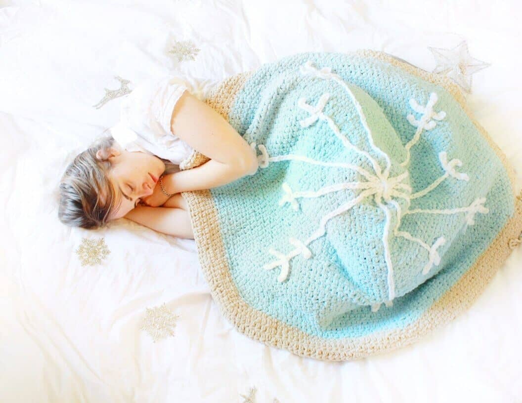 Photo of a sleeping woman covered with the Snowflake Sugar Cookie FREE Beginner Crochet Pattern