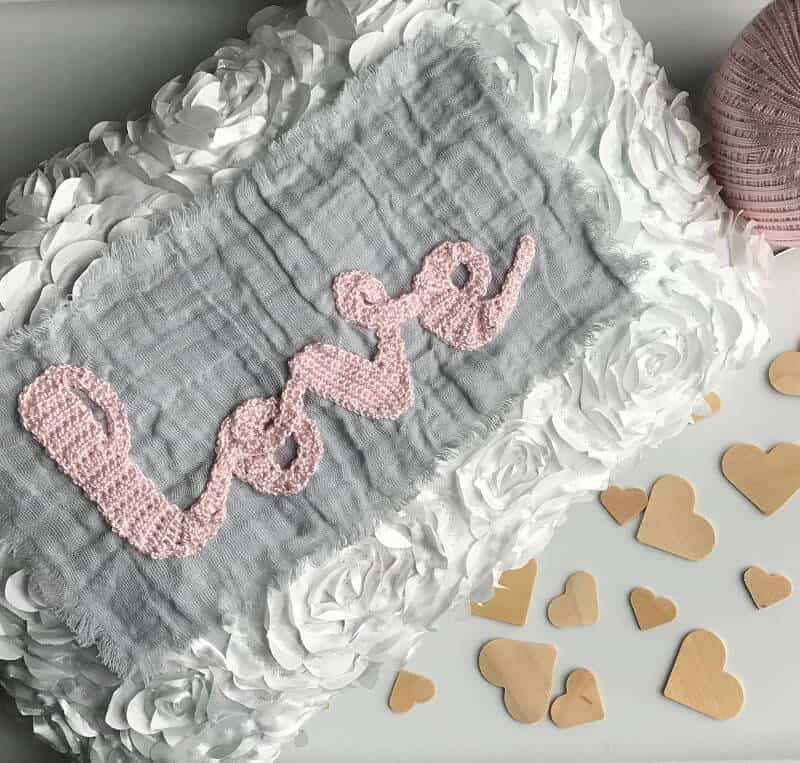 Photo of a white pillow with a crocheted text "love" on it