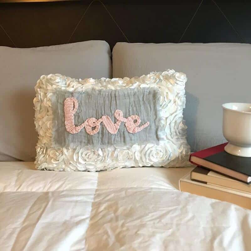 Photo of a white pillow with a crocheted text "love" on it.