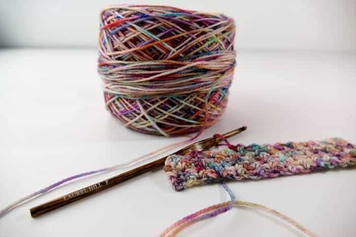 Photo of a ball of multicolored yarn, a small crocheted swatch, and a size F Laurel Hill Wooden Crochet Hook