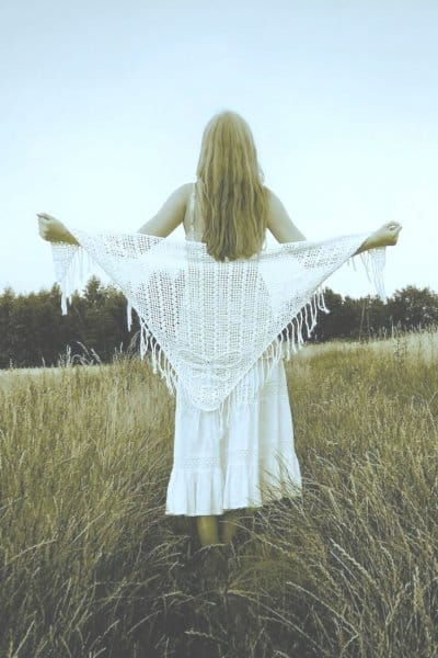 image of a woman in a field, from the rear, wearing a white crochet shawl