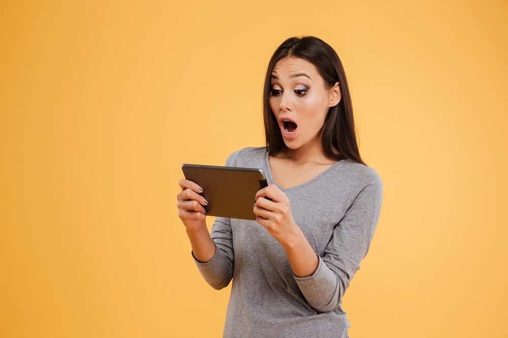 Photo of a woman holding an tablet wearing gray shirt with a surprised look
