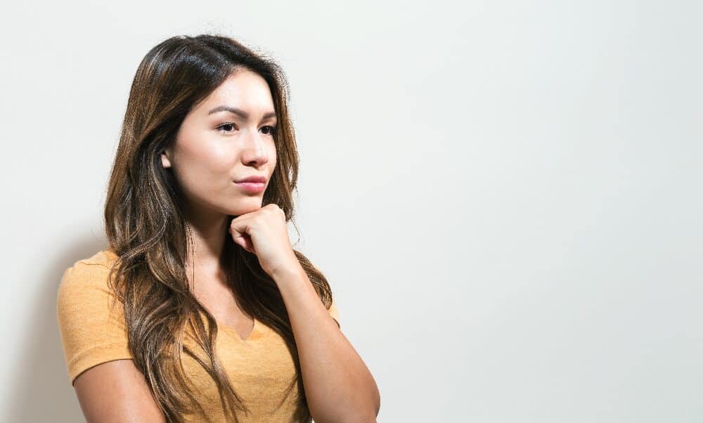 Image of a woman wearing a mustard-colored shirt with a thinking look