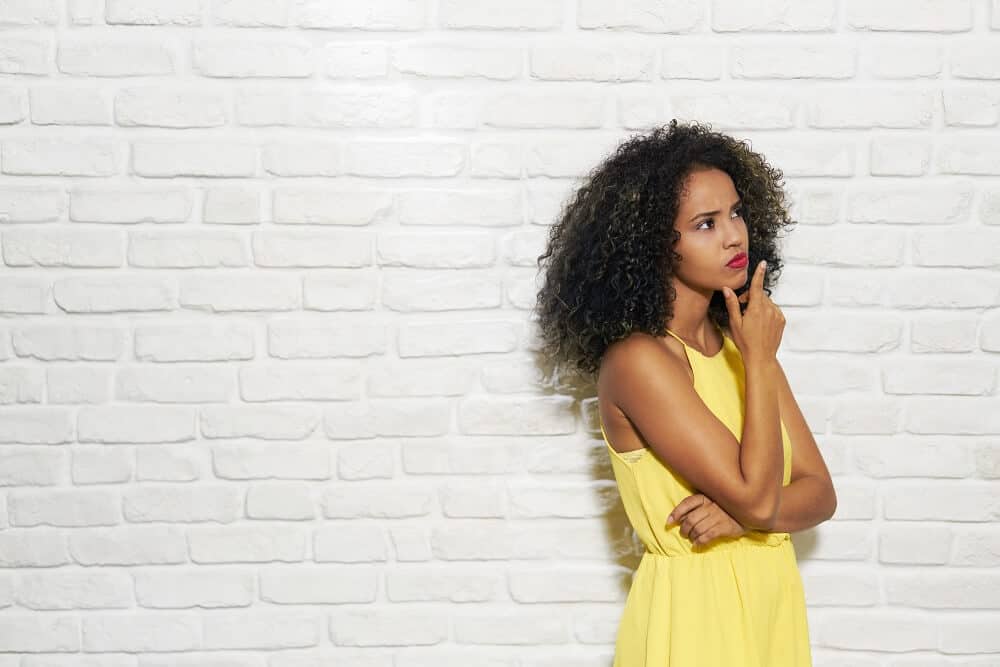 Photo of a woman with curly dark hair and wearing a yellow dress with a thinking look