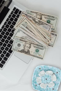 crochet blog hop - image of a laptop with a stack of bills on the keyboard, with a flower granny square nearby