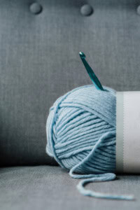 crochet business income - image of a ball of yarn laying on a couch, with a crochet hook sticking out of it