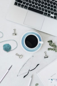 market your crochet business - image of a workspace with laptop, coffee mug, hooks, yarn, binder clips, and glasses