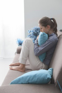 woman sitting alone on a couch, head down and hugging a pillow