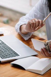using linkedin grow crochet business - woman sitting in front of a laptop, holding a pencil and a spiral notebook
