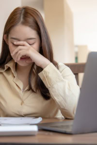 mistakes in crochet business - woman sitting in front of a laptop, eyes downcast with her hand covering her face