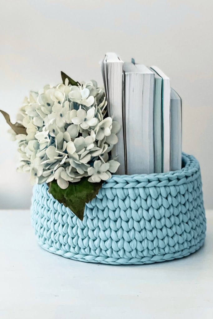 sell crochet items online - image of a crochet basket filled with a bunch of flowers and a stack of books