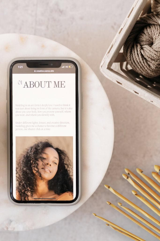 Crochet Business Branding Strategy Pin - Image featuring a cell phone displaying a woman's bio, a basket of yarn, and crochet hooks