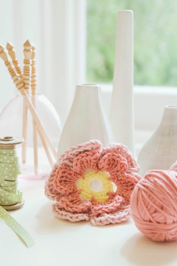 Crochet Craft Fair Ideas for Spring - image of decorative vases, one full of crochet hooks, a large crochet flower, and a ball of yarn