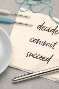 How to Make Crochet Business Successful - Image featuring a coffee cup, pen, crochet hook, yarn, and a note on a napkin that reads "decide, commit, succeed"