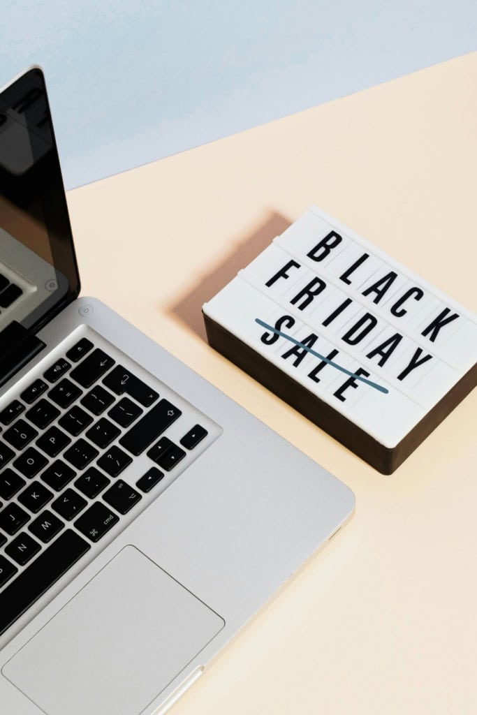 image of a laptop and folded bills, with a sign that reads "Black Friday Sale," with the word "sale" struck out