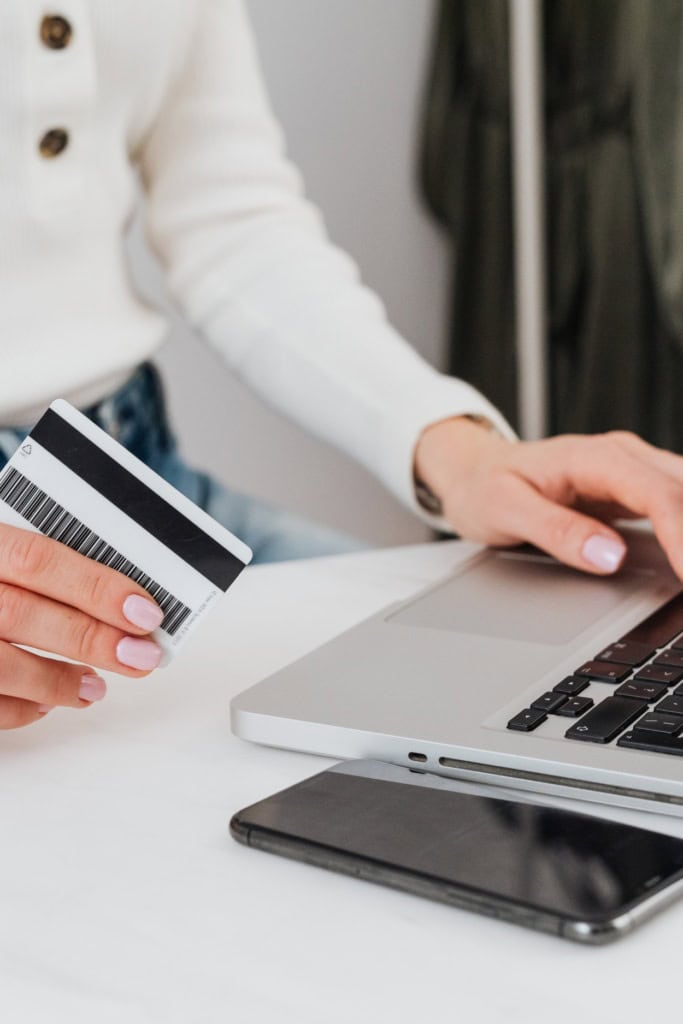 Woman's hand operating a laptop, holding a credit card in her other hand