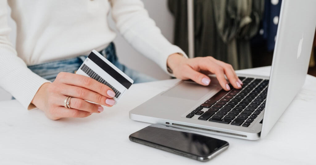 Woman's hand operating a laptop, holding a credit card in her other hand