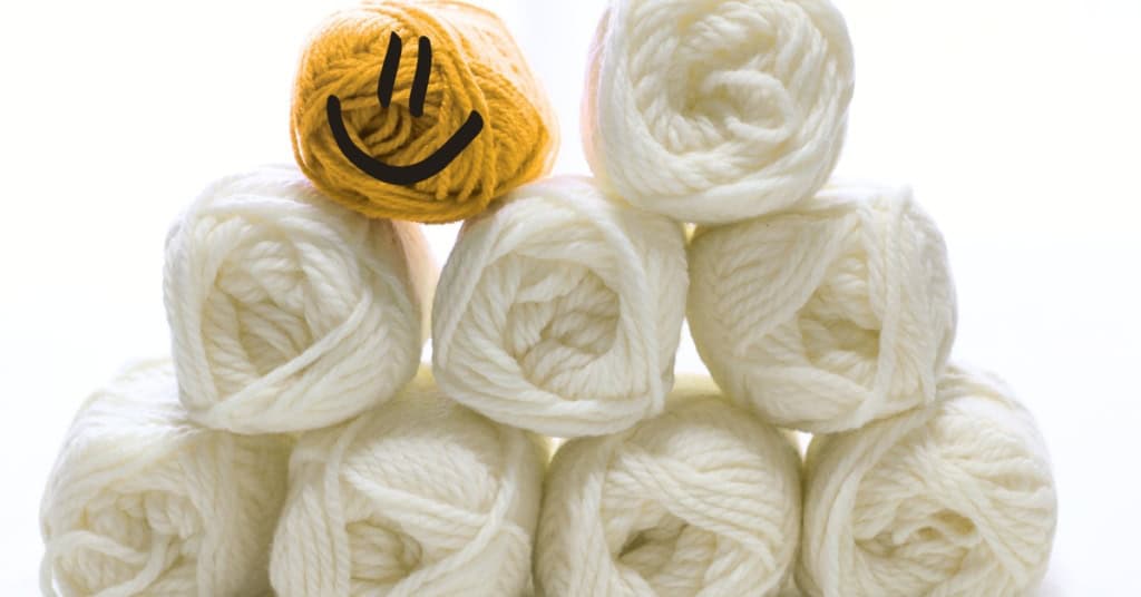 A stack of yarn, all white skeins except one yellow skein, which has a smiling face