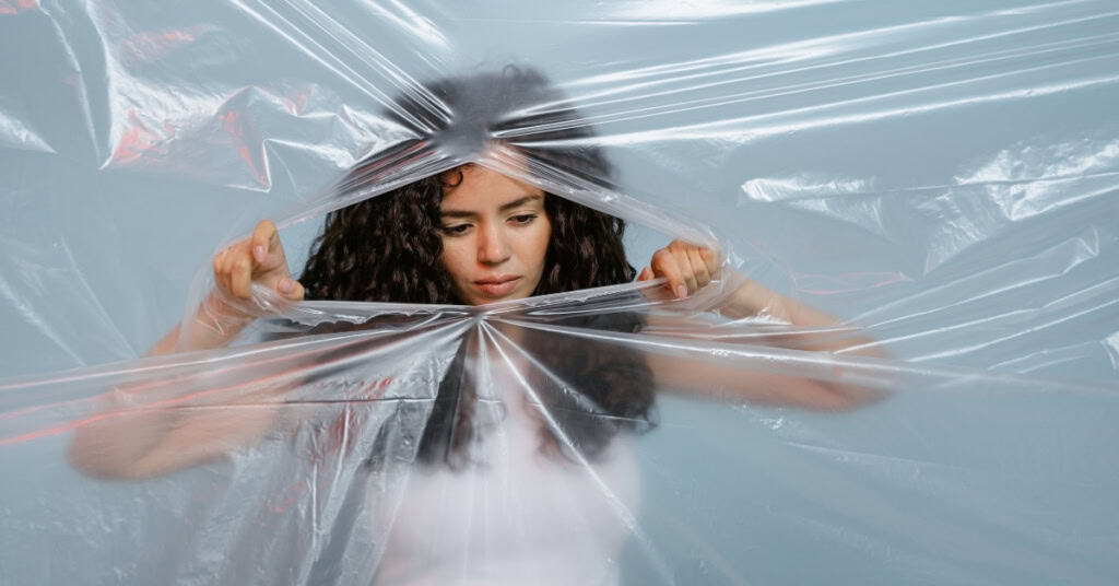 A woman tearing through a translucent plastic sheet, symbolizing breaking through the rules associated with crochet business.