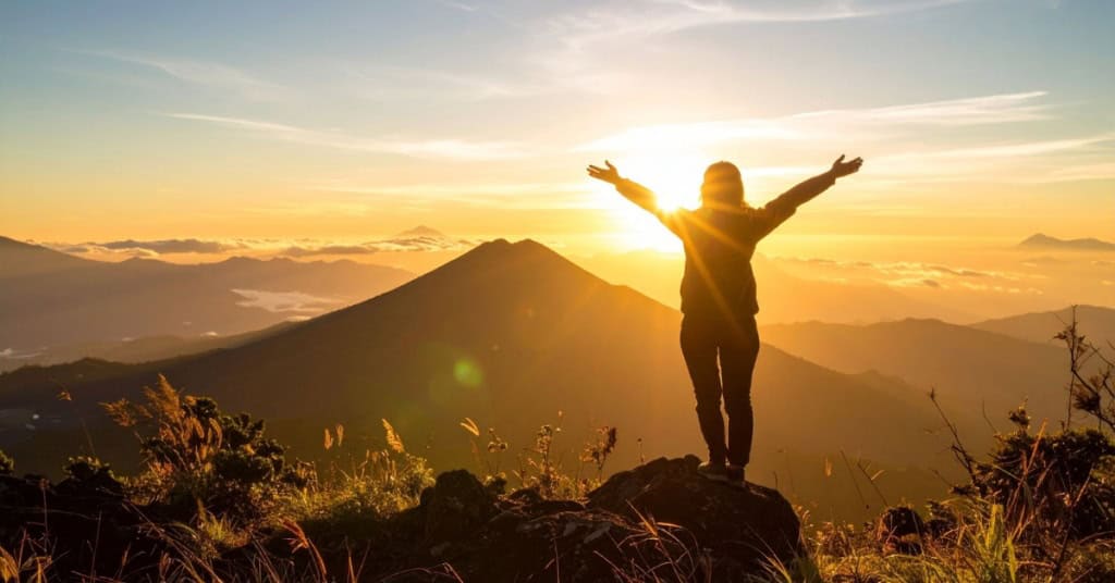 A woman standing with arms wide open on a mountain top at sunset, embodying the freedom you feel when you break the rules in your crochet business.
