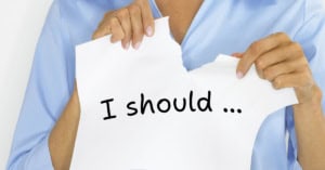 Image of a woman tearing a piece of paper with her hands, on which is written "I should ..."