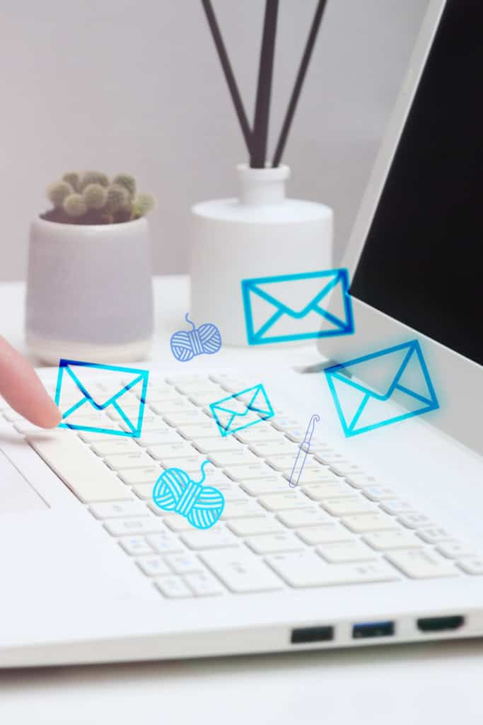 Open laptop with small envelopes, skeins of yarn and a crochet hook "flying" out of the screen